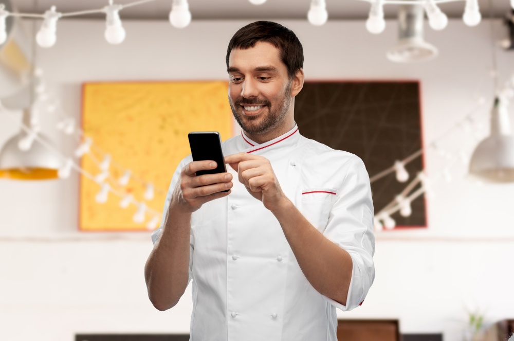 cooking, culinary and people concept - happy smiling male chef with smartphone over restaurant background. happy smiling male chef with smartphone