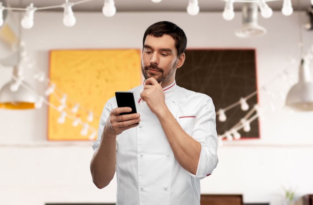 cooking, culinary and people concept - thinking male chef with smartphone over restaurant background. thinking male chef with smartphone