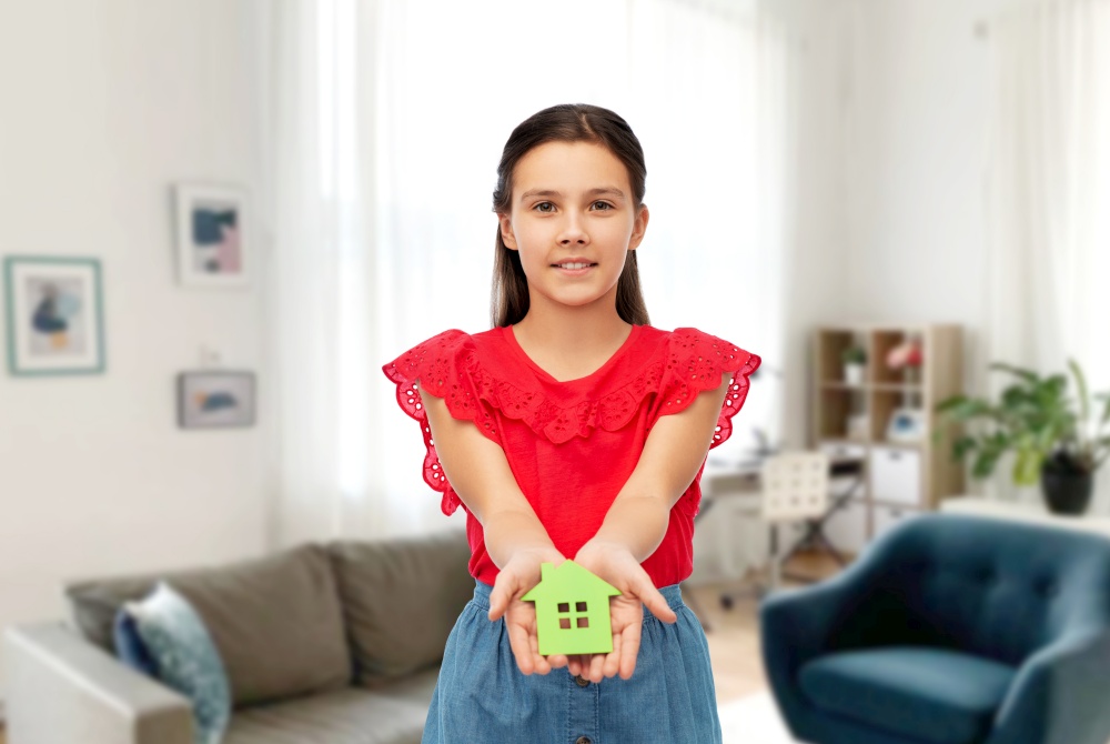 eco living, environment and sustainability concept - smiling little girl holding green house icon over home background. smiling girl holding green house icon at home