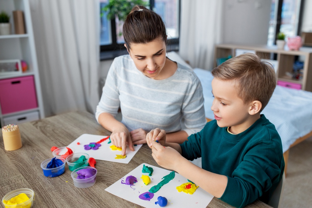 family, creativity and craft concept - mother and little son making picture of modeling clay at home. mother and son playing with modeling clay at home
