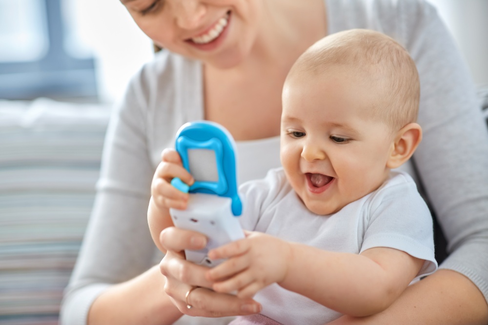 family, motherhood and people concept - happy smiling mother and little baby playing with toy phone at home. mother with baby playing with toy phone at home