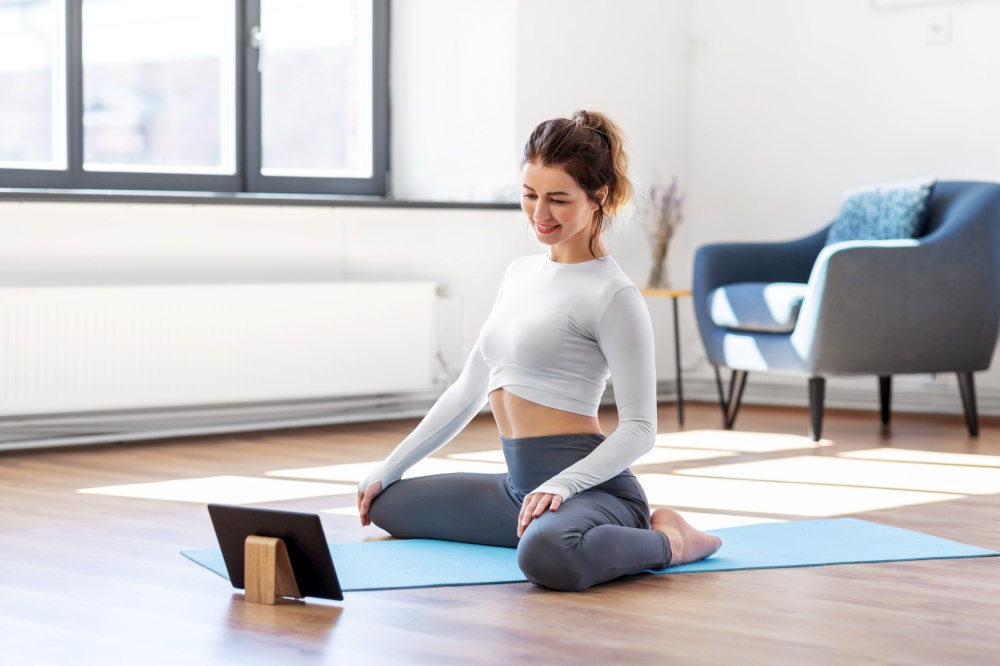 fitness, people and healthy lifestyle concept - young woman with tablet pc computer doing yoga at home. young woman with tablet pc doing yoga at home