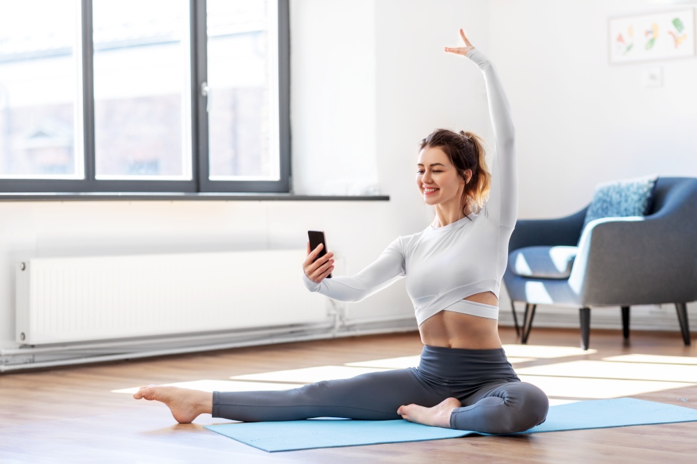 fitness, people and healthy lifestyle concept - young woman with smartphone doing yoga at home. young woman with smartphone doing yoga at home