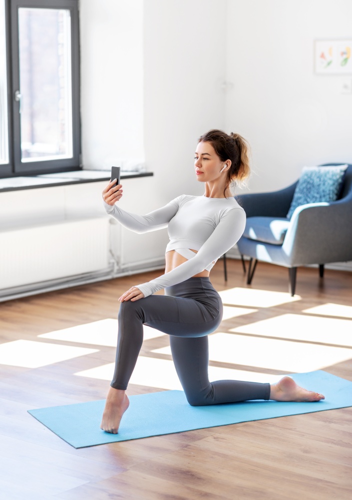 fitness, people and healthy lifestyle concept - young woman with smartphone and earphones doing yoga at home. young woman with smartphone doing yoga at home