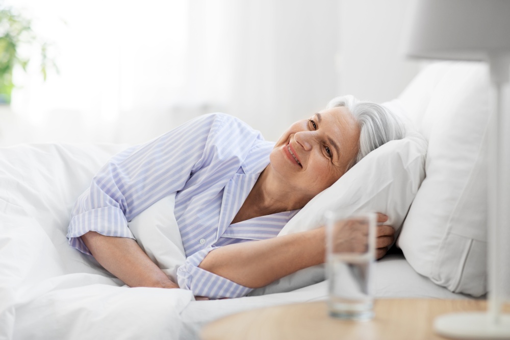 old age and people concept - happy smiling senior woman lying in bed at home bedroom. happy senior woman lying in bed at home bedroom