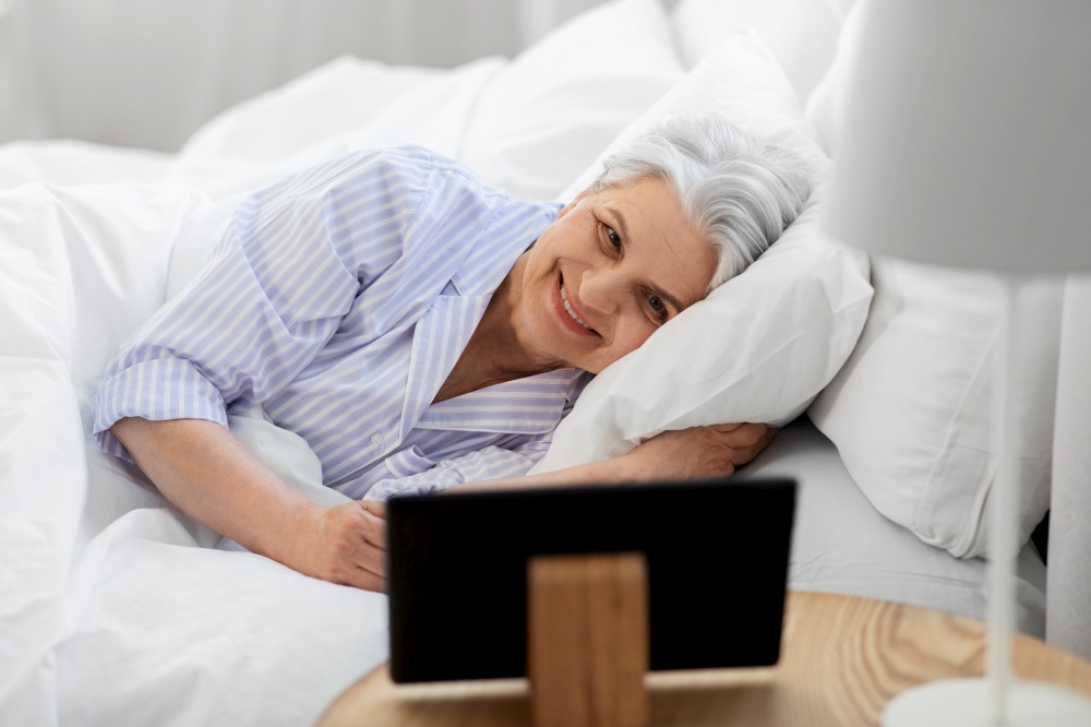 old age and people concept - happy smiling senior woman with tablet pc lying in bed at home bedroom. happy senior woman with tablet pc in bed at home