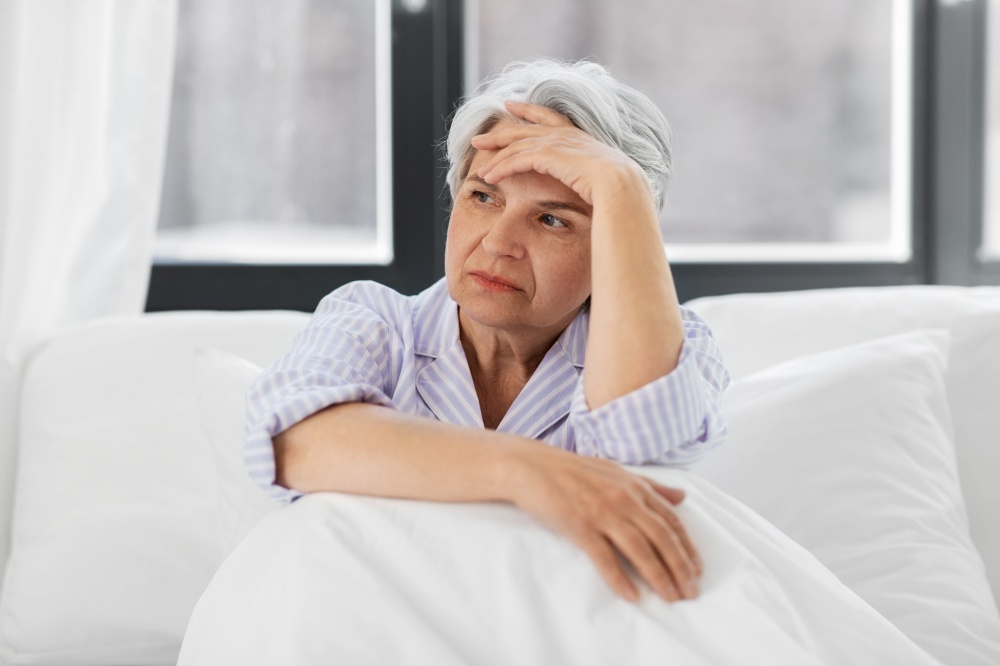 health, old age and people concept - senior woman in pajamas suffering from headache sitting in bed at home bedroom. senior woman with headache sitting in bed at home