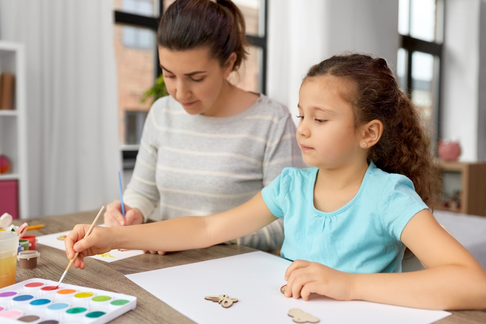 family, motherhood and leisure concept - mother spending time with her little daughter drawing or painting wooden chipboard items with colors at home. mother with little daughter drawing at home