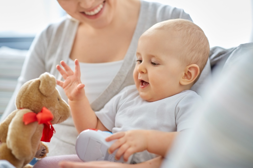 family, motherhood and people concept - close up of happy smiling mother and little baby playing with teddy bear toy at home. close up of mother with little baby at home