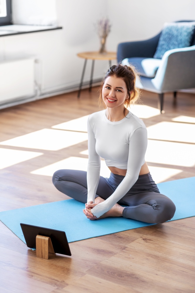 fitness, people and healthy lifestyle concept - young woman with tablet pc computer doing yoga at home. young woman with tablet pc doing yoga at home