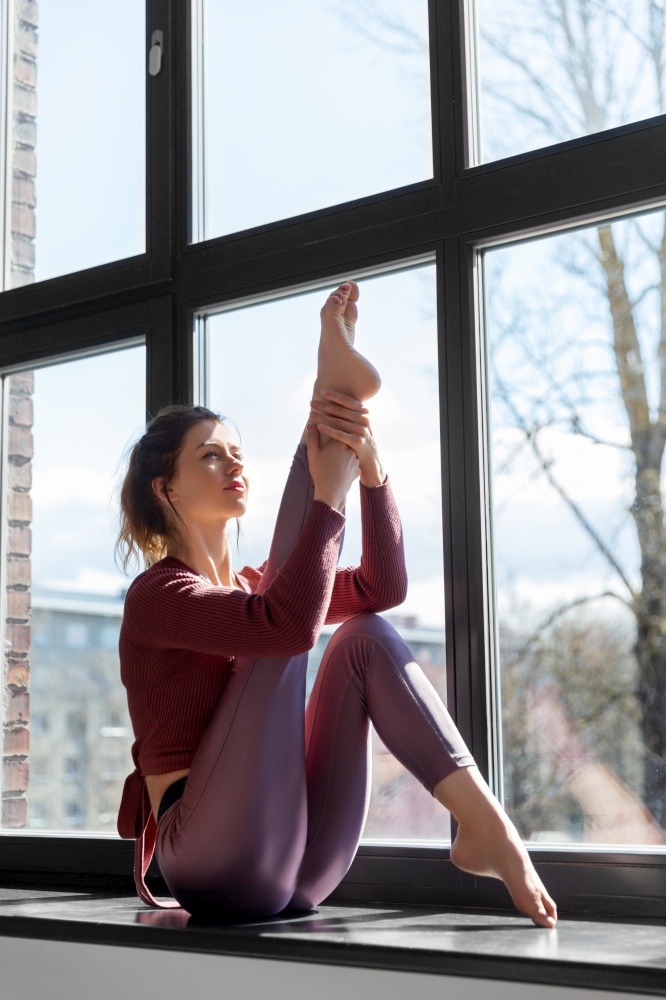 fitness, sport and healthy lifestyle concept - woman doing yoga exercise on window sill at studio. woman doing yoga exercise on window sill at studio