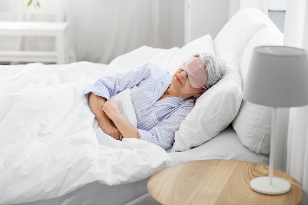 old age and people concept - senior woman with eye mask sleeping in bed at home bedroom. senior woman with eye mask sleeping in bed at home
