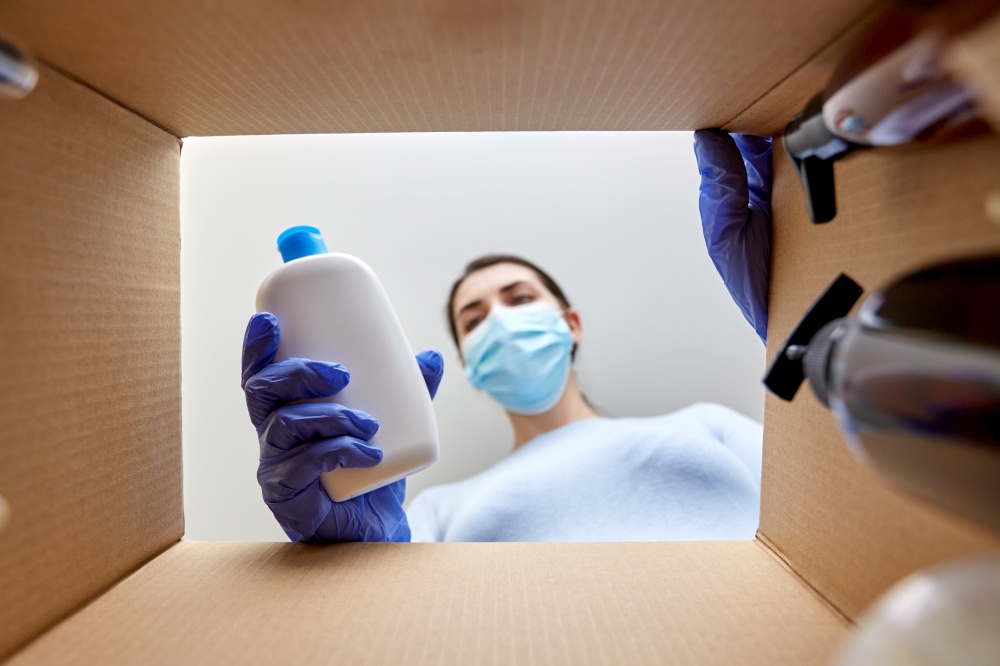 home delivery, shipping and pandemic concept - woman in protective medical mask and gloves unpacking parcel box with cosmetics and beauty products. woman in mask unpacking parcel box with cosmetics