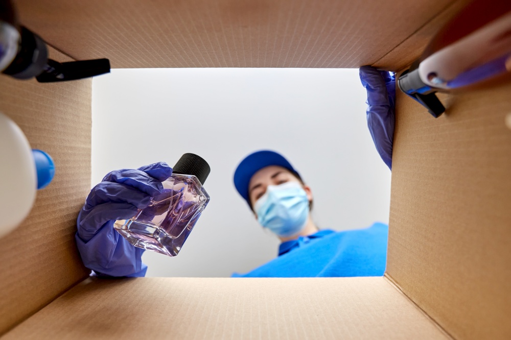 home delivery, shipping and pandemic concept - woman in protective medical mask and gloves packing parcel box with perfume and beauty products. woman in mask packing parcel box with cosmetics