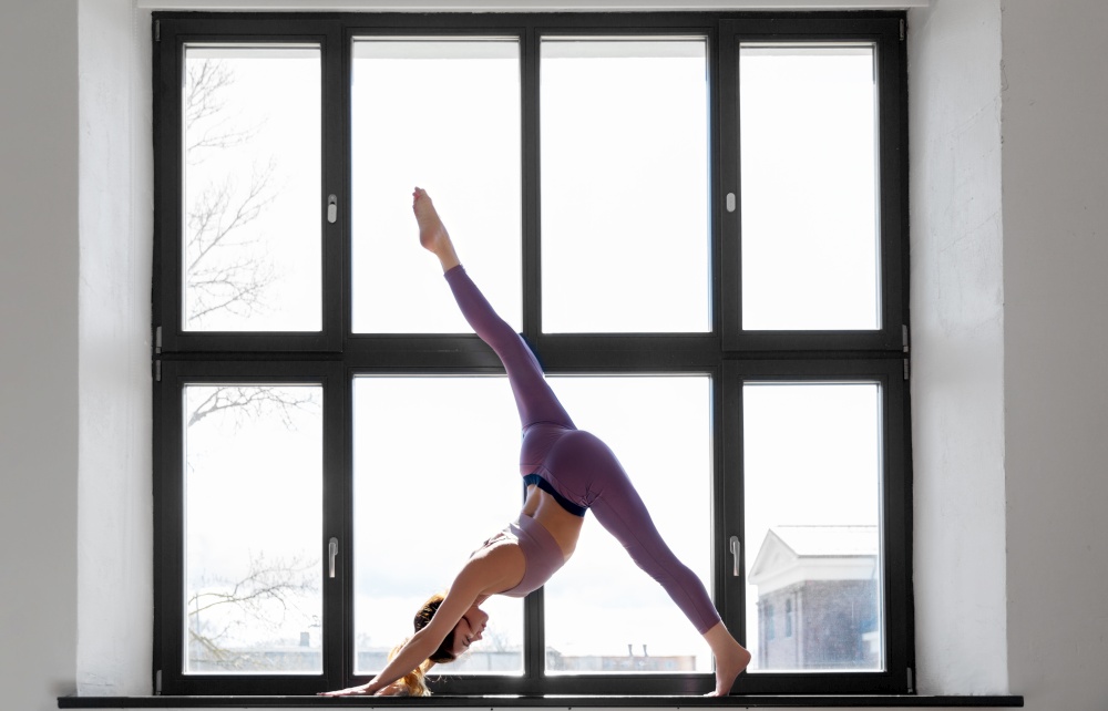 fitness, sport and healthy lifestyle concept - woman doing yoga exercise on window sill at studio. woman doing yoga exercise on window sill at studio