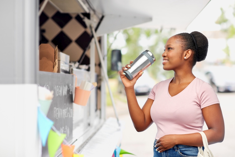 sustainability and people concept - happy african american woman with thermo cup or tumbler for hot drinks and food in string bag over food truck background. woman with tumbler and food in string bag