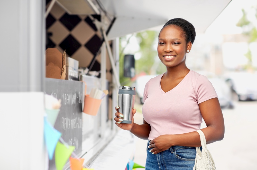 sustainability and people concept - happy african american woman with thermo cup or tumbler for hot drinks and food in string bag over food truck background. woman with tumbler and food in string bag