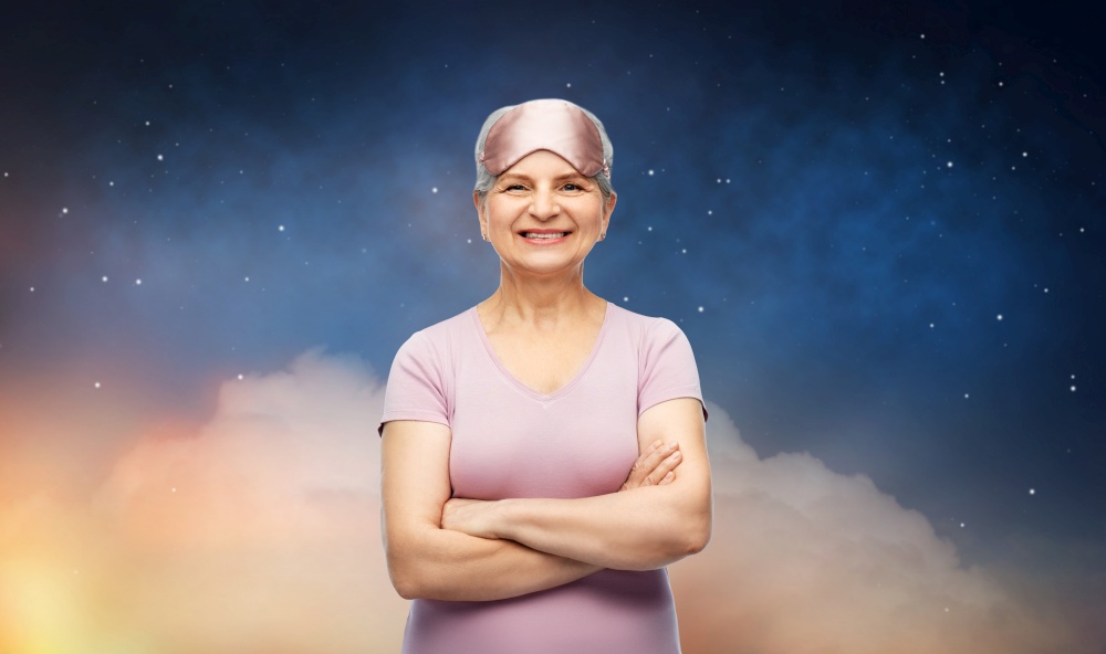 bedtime, rest and old people concept - portrait of smiling senior woman in pajamas and eye sleeping mask with crossed arms over starry night sky background. senior woman in pajamas and eye sleeping mask