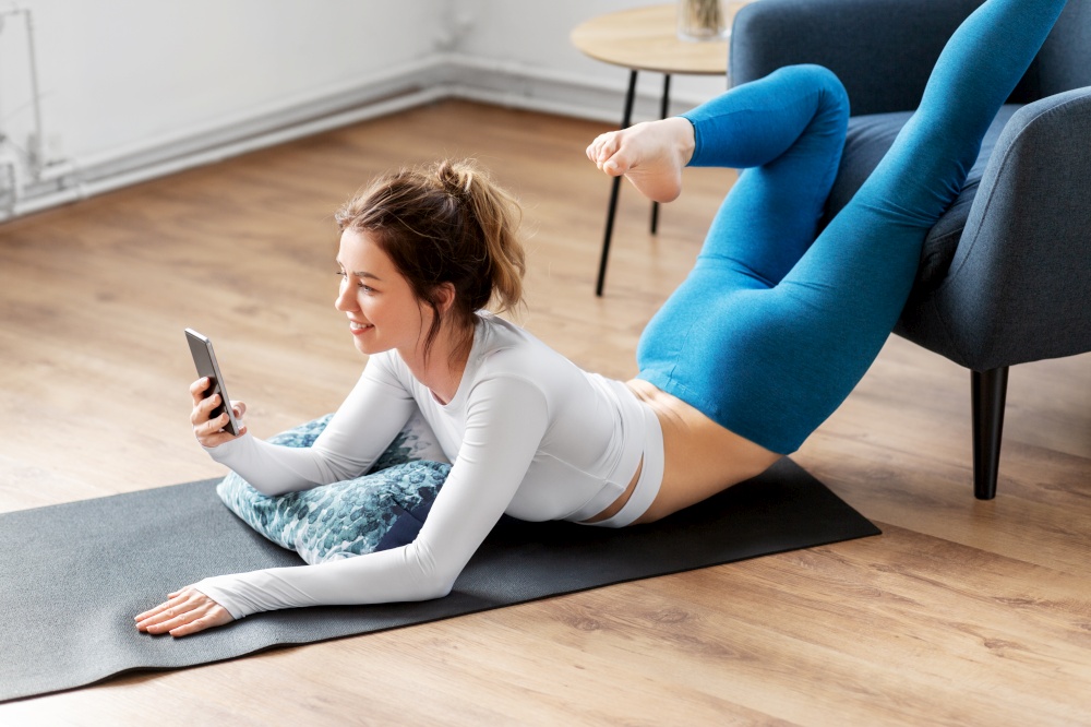 fitness, yoga and healthy lifestyle concept - young woman with smartphone stretching at home. woman with smartphone stretching yoga at home