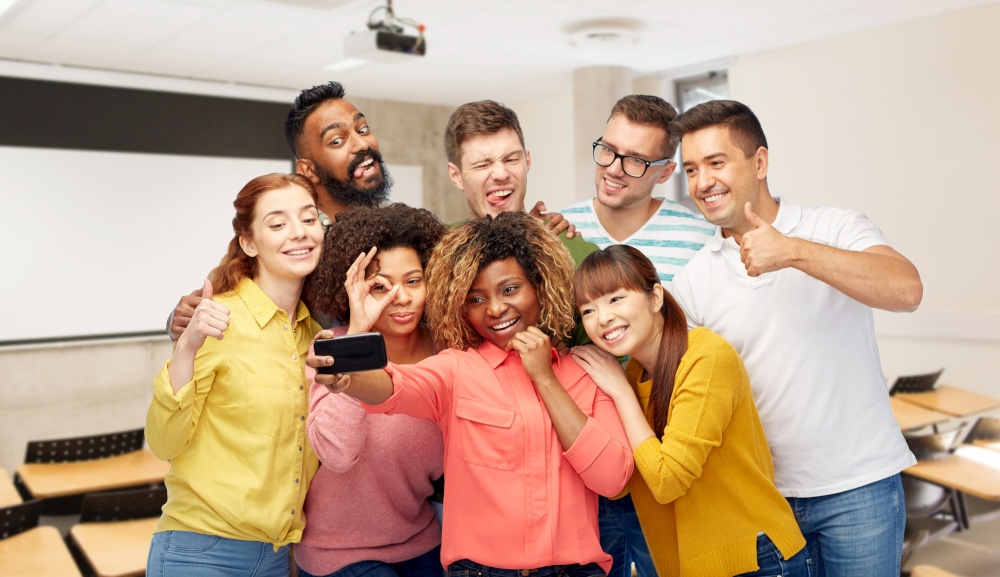 diversity, education and school concept - group of smiling international university students and teacher taking selfie with smartphone over lecture hall on background. international students and teacher taking selfie