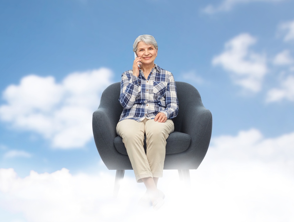communication, technology and old people concept - smiling senior woman sitting in modern armchair and calling on smartphone over blue sky and clouds background. senior woman calling on smartphone in armchair