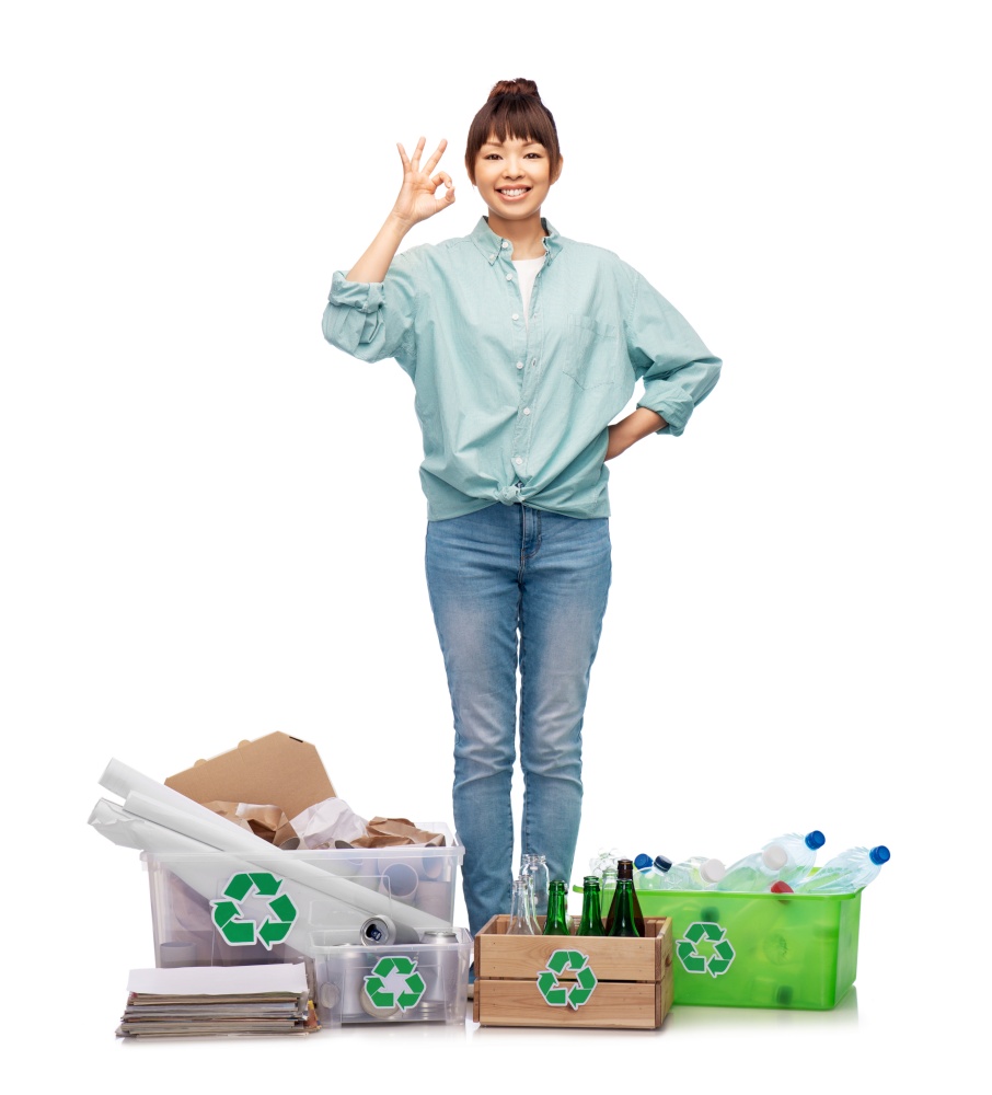 recycling, waste sorting and sustainability concept - smiling young asian woman with plastic and glass bottles, papers and metal tin cans in boxes showing ok gesture over white background. happy woman sorting paper, metal and plastic waste