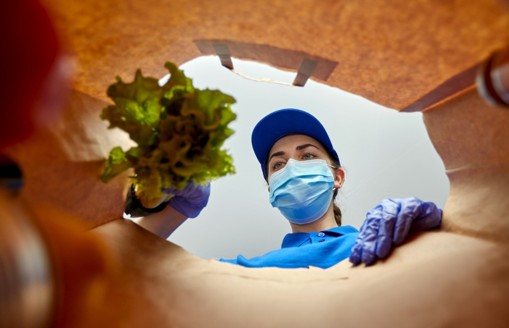 health protection and pandemic concept - female delivery worker in protective medical gloves and mask packing food into paper bag. delivery girl in gloves and mask with food in bag