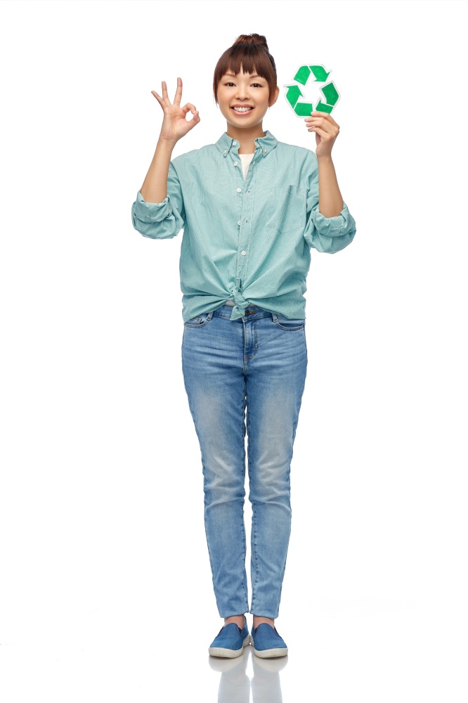 eco living, environment and sustainability concept - portrait of happy smiling young asian woman in turquoise shirt holding green recycling sign showing ok hand sign over white background. smiling asian woman holding green recycling sign