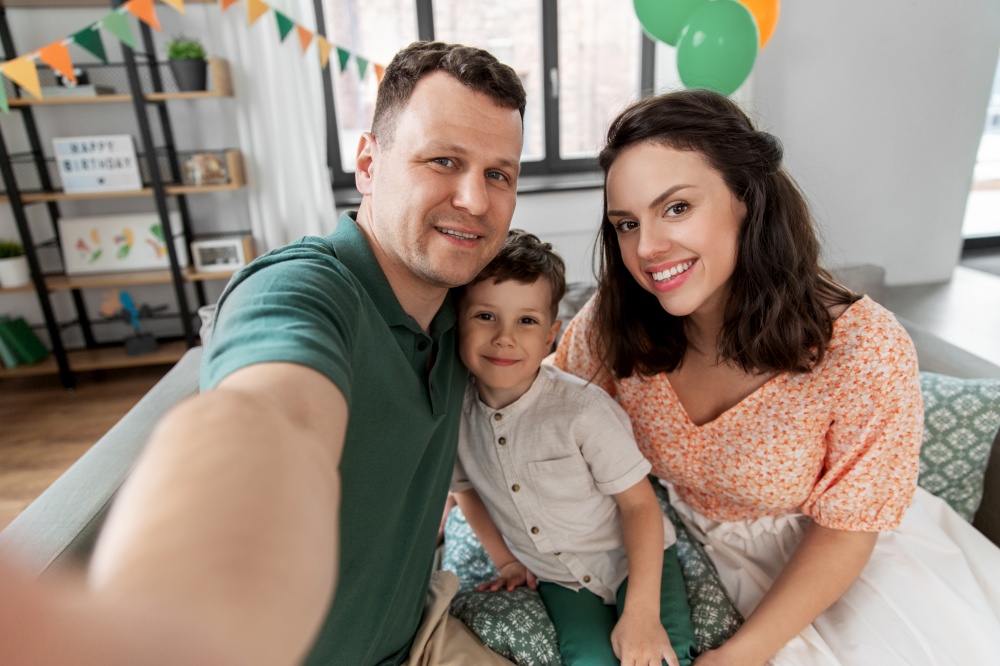 family, holidays and people concept - portrait of happy mother, father and little son taking selfie on birthday at home party. happy family taking selfie on birthday at home