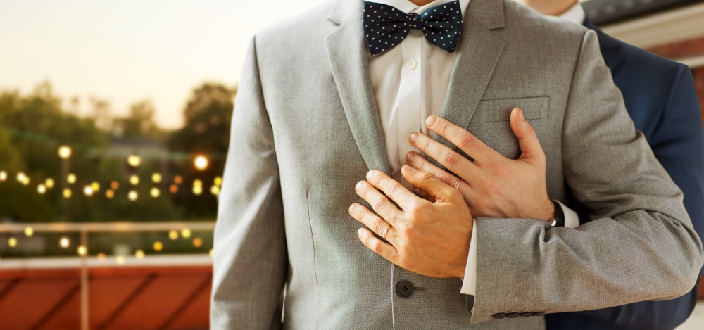 homosexuality, same-sex marriage and lgbt concept - close up of happy male gay couple with wedding rings hugging over roof top party background. close up of male gay couple with wedding rings on