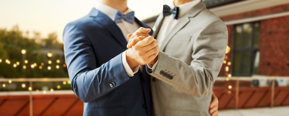 homosexuality, same-sex marriage and lgbt concept - close up of happy male gay couple holding hands and dancing on wedding over roof top party background. close up of happy male gay couple dancing at party
