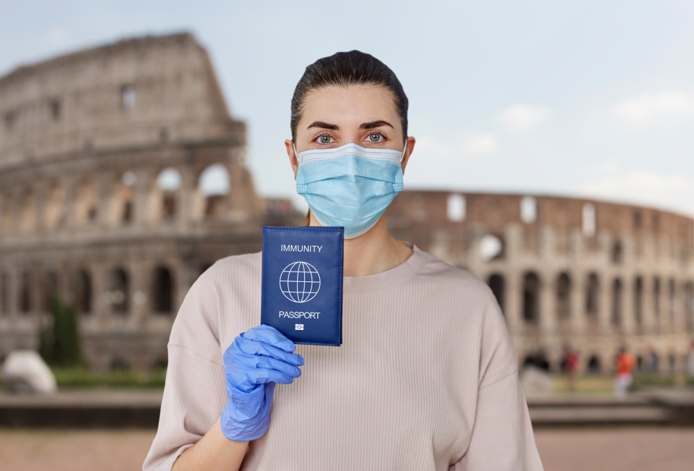 health protection, vaccination and pandemic concept - close up of young woman in medical mask and gloves holding immunity passport over colosseum in rome, italy on background. woman in mask and gloves holding immunity passport