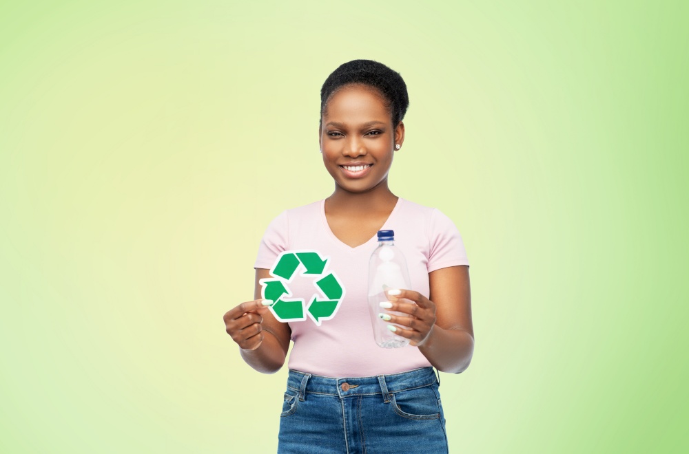 eco living, environment and sustainability concept - smiling young african american woman holding recycling sign and plastic bottle over green background. woman with recycling sign and plastic bottle