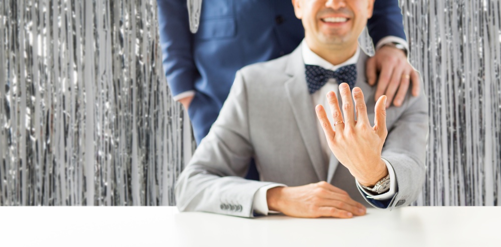 homosexuality, same-sex marriage and lgbt concept - close up of male gay couple with wedding rings on putting hand on shoulder over foil party curtain on background. close up of male gay couple with wedding rings on