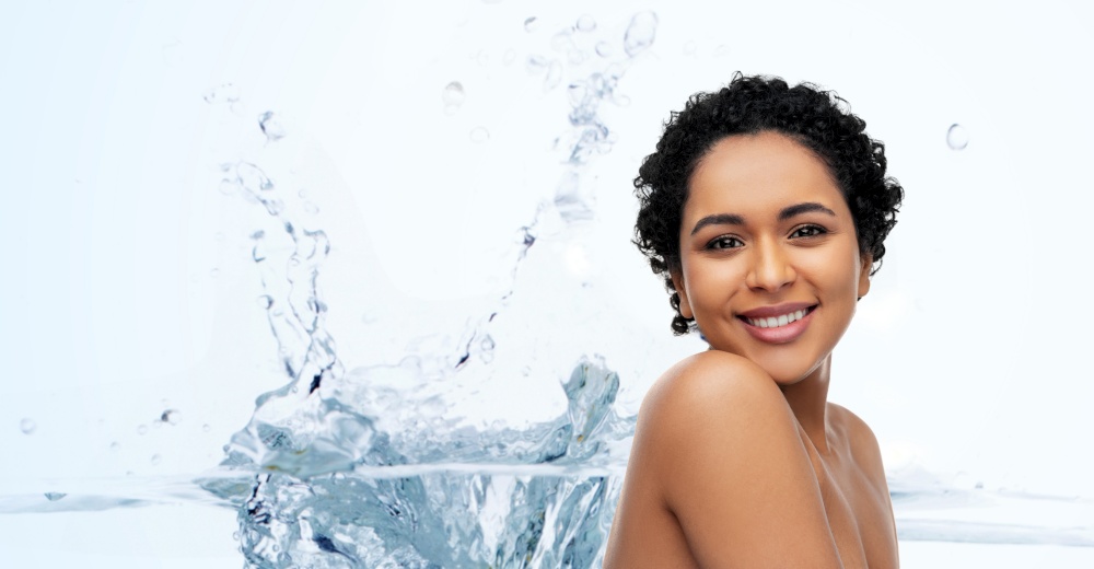 beauty and people concept - portrait of happy smiling young african american woman with bare shoulders over water splash on blue background. portrait of young african american woman