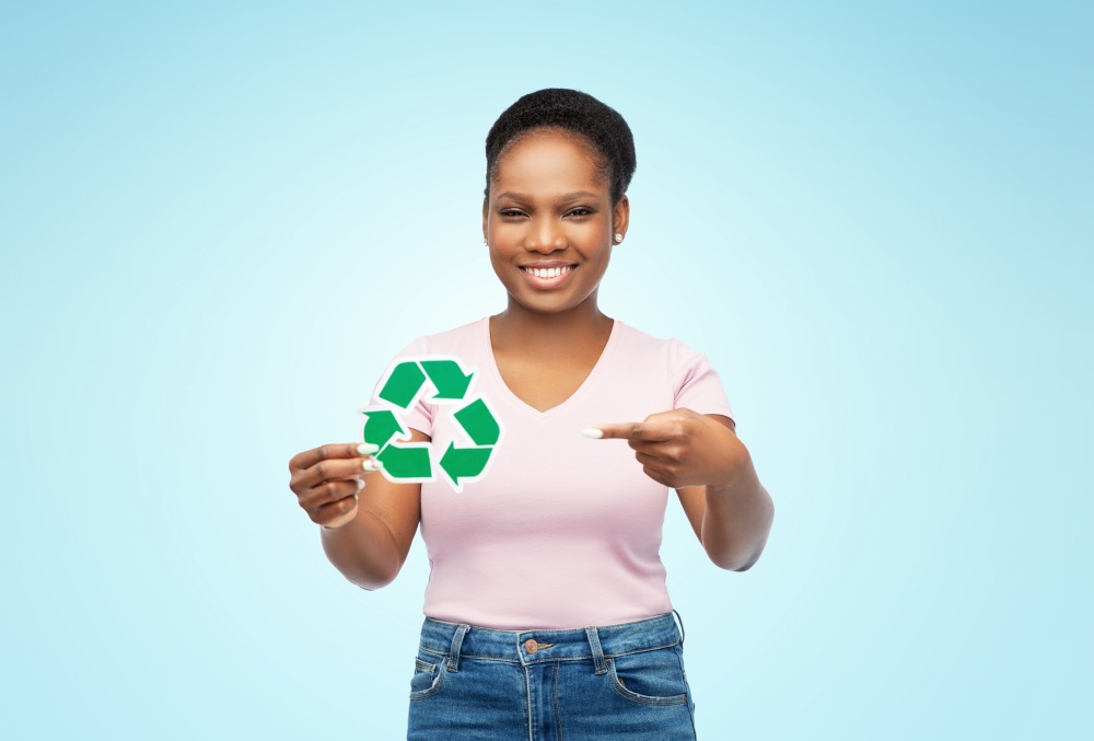 eco living, environment and sustainability concept - portrait of happy smiling young african american woman holding green recycling sign over blue background. smiling asian woman holding green recycling sign