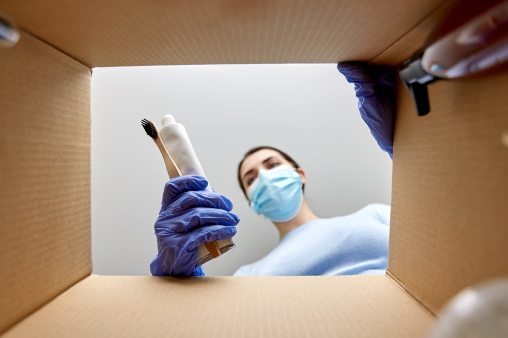 home delivery, shipping and pandemic concept - woman in protective medical mask and gloves unpacking parcel box with cosmetics and beauty products. woman in mask unpacking parcel box with cosmetics