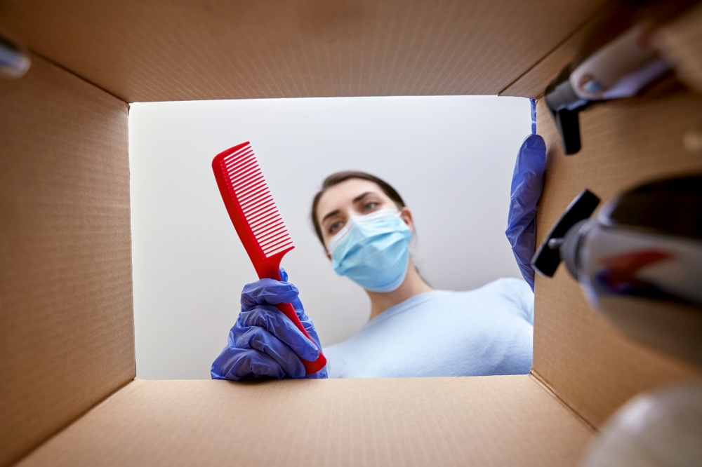 home delivery, shipping and pandemic concept - woman in protective medical mask and gloves unpacking parcel box with comb and beauty products. woman in mask unpacking parcel box with cosmetics