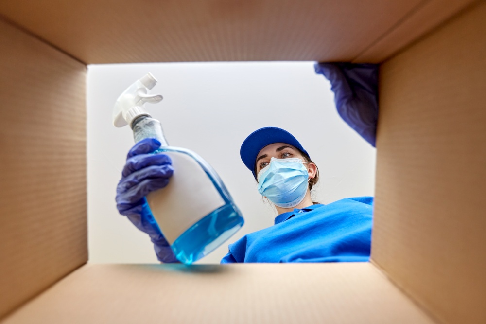 delivery, shipping and pandemic concept - woman in protective medical mask and gloves packing cleaning supplies to parcel box. woman in mask packing cleaning supplies in box