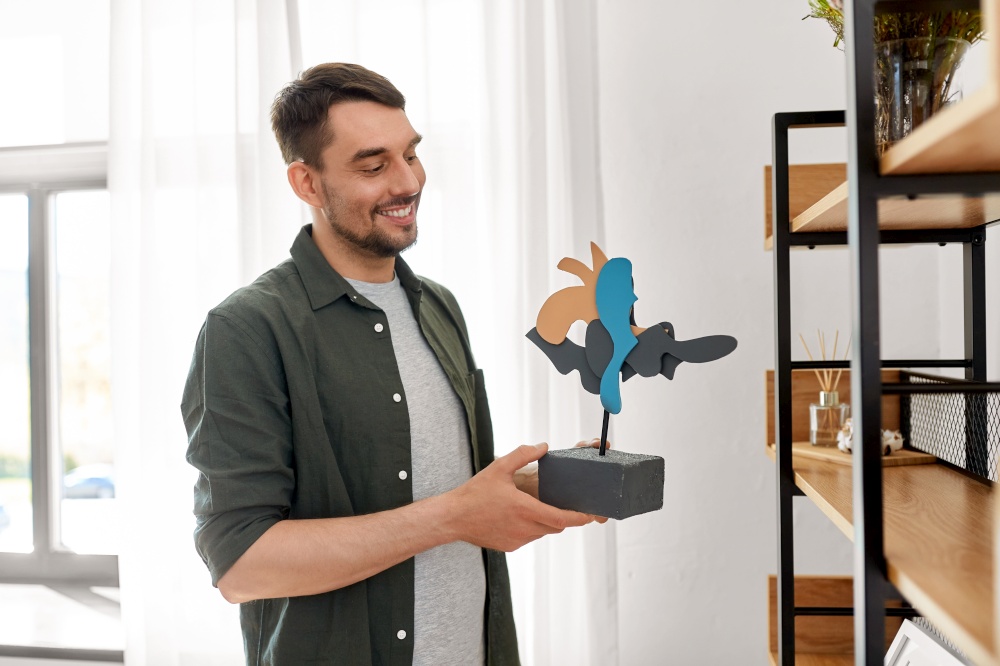 home improvement, decoration and people concept - happy smiling man placing art to shelf. man decorating home with art in frame