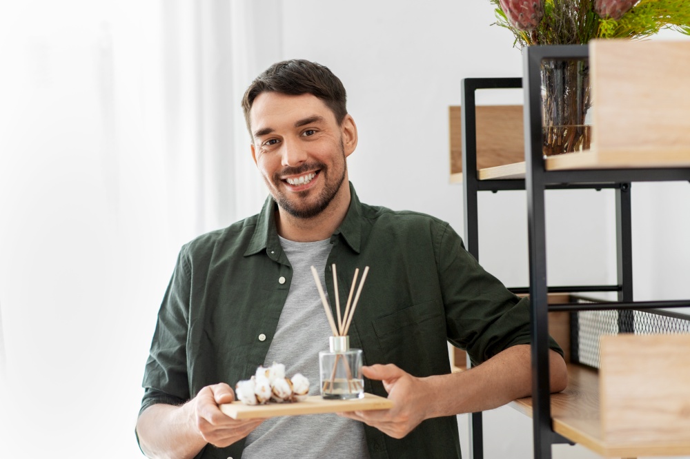 home improvement, decoration and people concept - happy smiling man placing aroma reed diffuser and cotton flowers to shelf. man placing aroma reed diffuser to shelf home