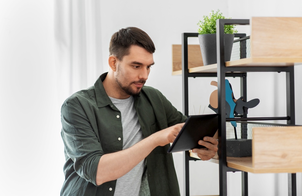 home improvement and decoration and people concept - man with tablet pc computer standing at shelf at home. man with tablet pc at shelf at home