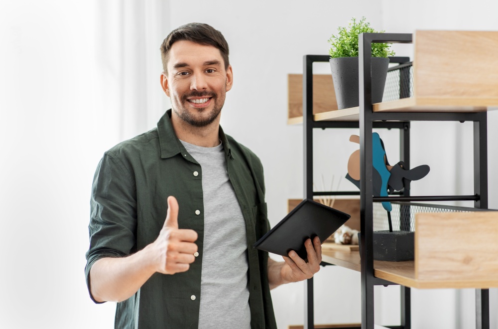 home improvement and decoration and people concept - happy smiling man with tablet pc computer showing thumbs up standing at shelf at home. happy smiling man with tablet pc at shelf at home