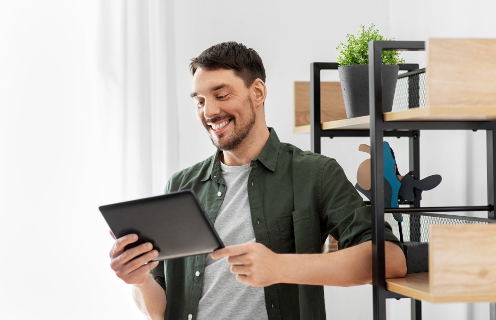 home improvement and decoration and people concept - happy smiling man with tablet pc computer standing at shelf at home. happy smiling man with tablet pc at shelf at home