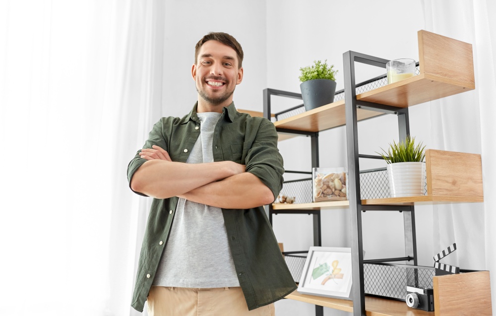 home improvement and decoration and people concept - happy smiling man with crossed arms standing at shelf. happy smiling man with crossed arms at home