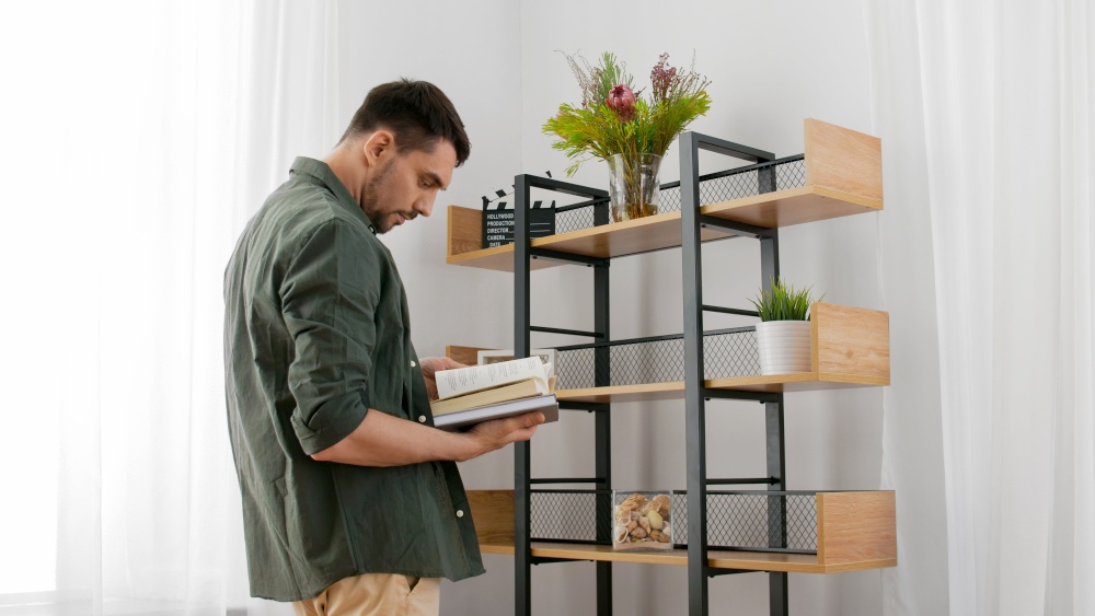 home improvement and decoration and people concept - man with books arranging shelf. man with books decorating home and arranging shelf