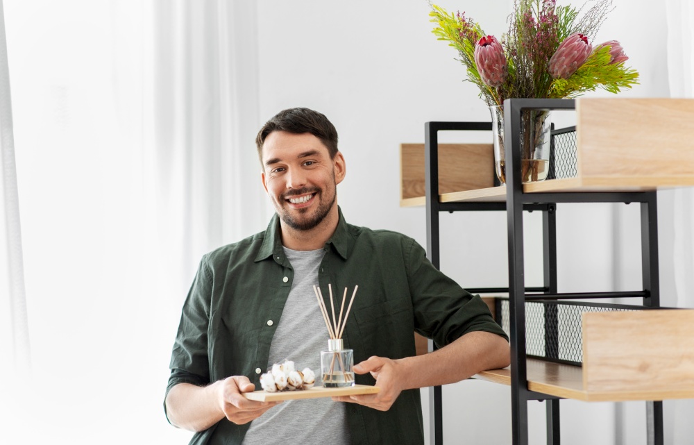 home improvement, decoration and people concept - happy smiling man placing aroma reed diffuser and cotton flowers to shelf. man placing aroma reed diffuser to shelf home