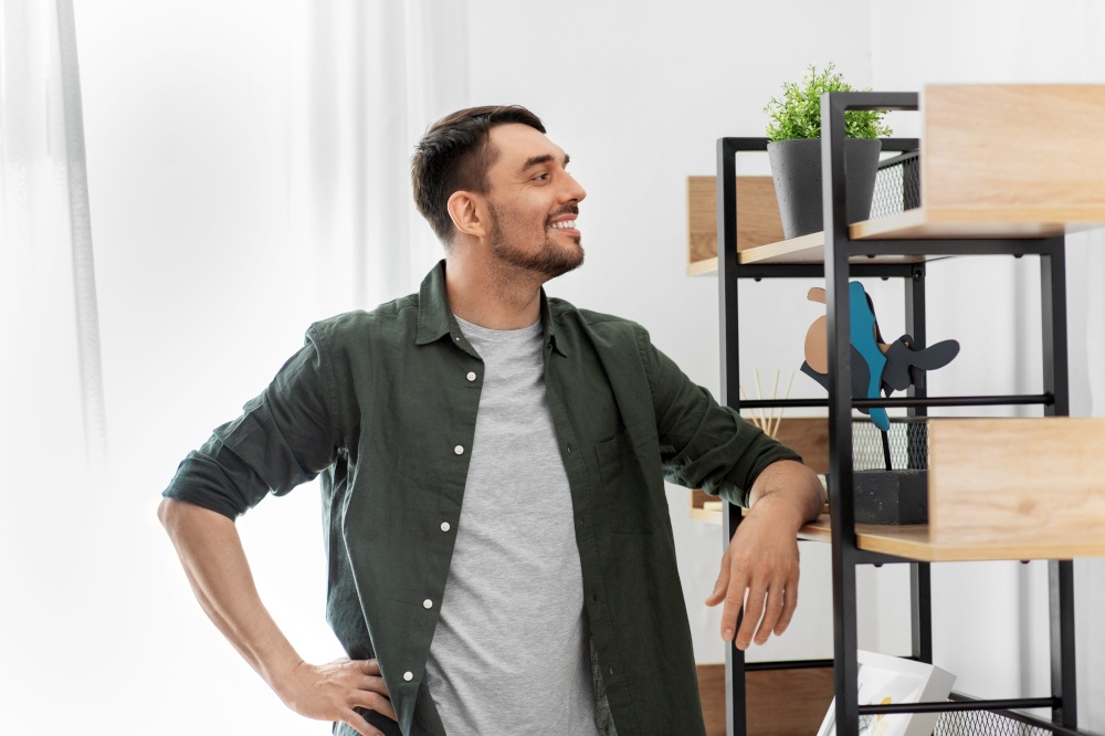 home improvement and decoration and people concept - happy smiling man standing at shelf at home. happy smiling man standing at shelf at home