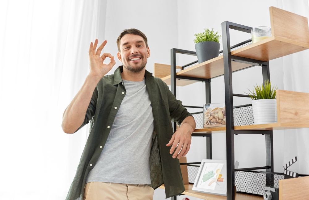 home improvement and decoration and people concept - happy smiling man standing at shelf showing ok hand sign. happy smiling man standing at shelf at home