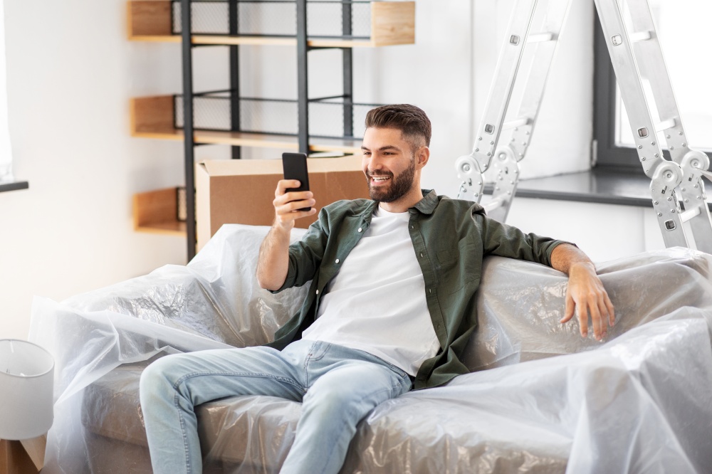 moving, people and real estate concept - happy smiling man with smartphone and boxes at new home. man with smartphone and boxes moving into new home